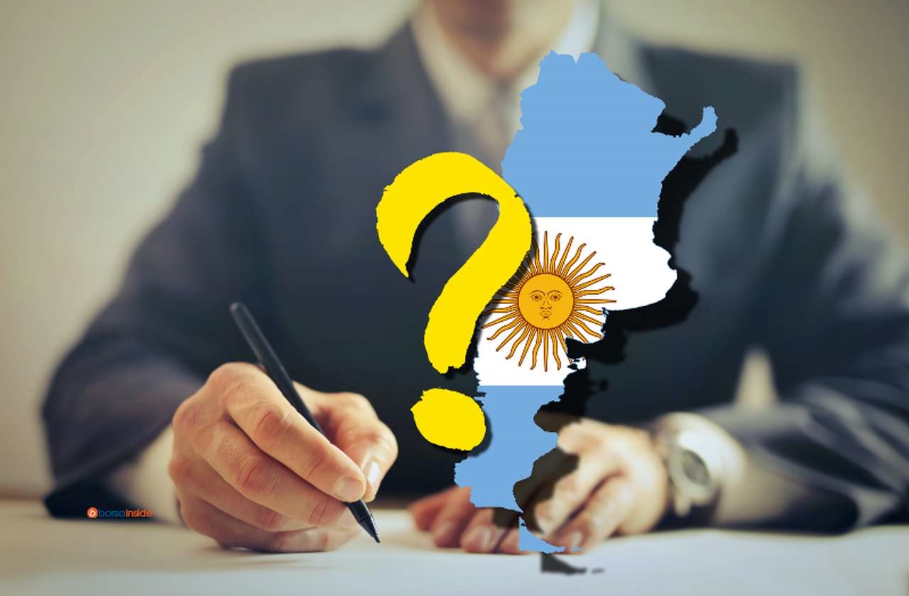 Il primo piano di un uomo in giacca e cravatta che appone una firma, con la bandiera dell'Argentina racchiusa nei confini dello Stato e un punto interrogativo in sovrimpressione