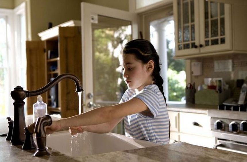 una ragazzina che apre il rubinetto dell'acqua in cucina