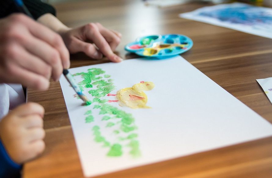 un foglio con un dipinto su un tavolo di legno e le mani di un bambino e della maestra