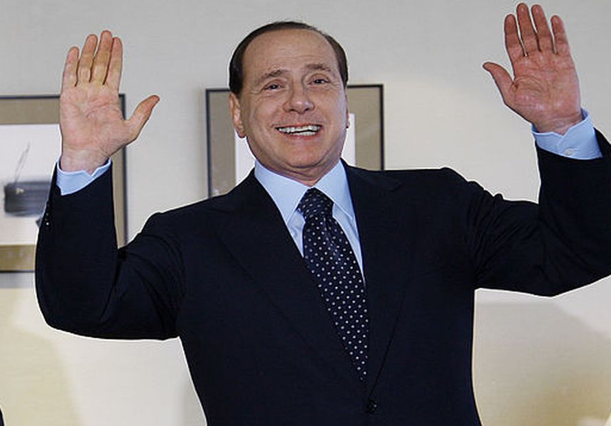 Berlusconi a mezzo busto che sorride con le mani alzate