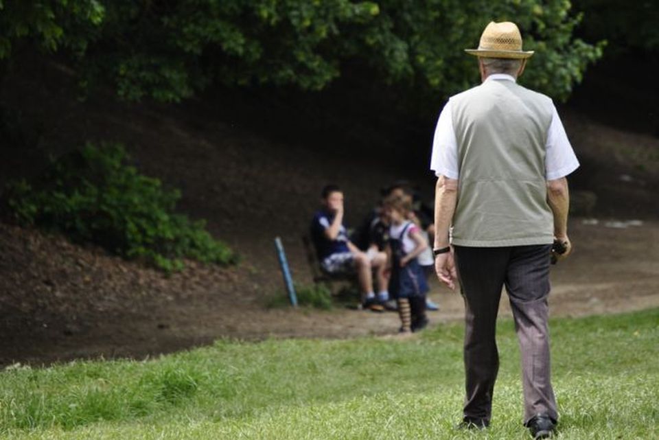 un signore di mezza età visto di spalle mentre cammina sul prato in un parco pubblico