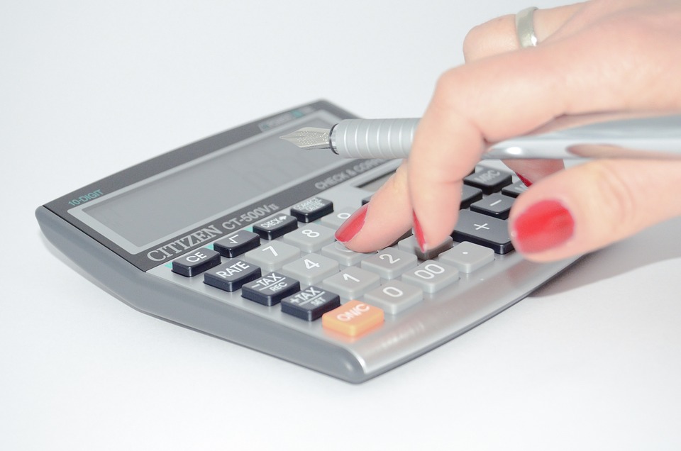 la mano di una donna che impugna una penna e digita su una calcolatrice tascabile