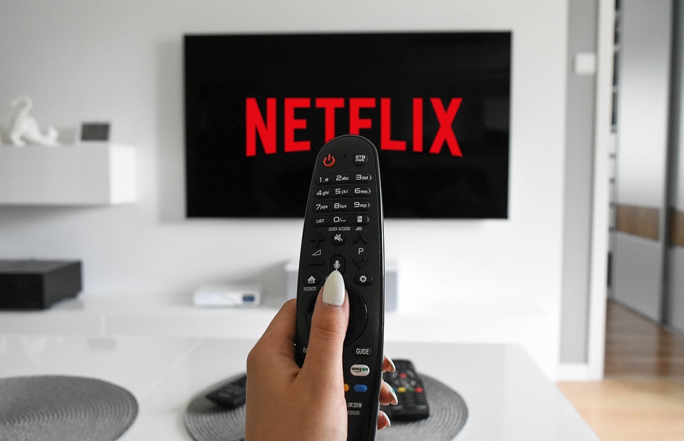 una tv accesa con scritta Netflix e una mano femminile con il telecomando