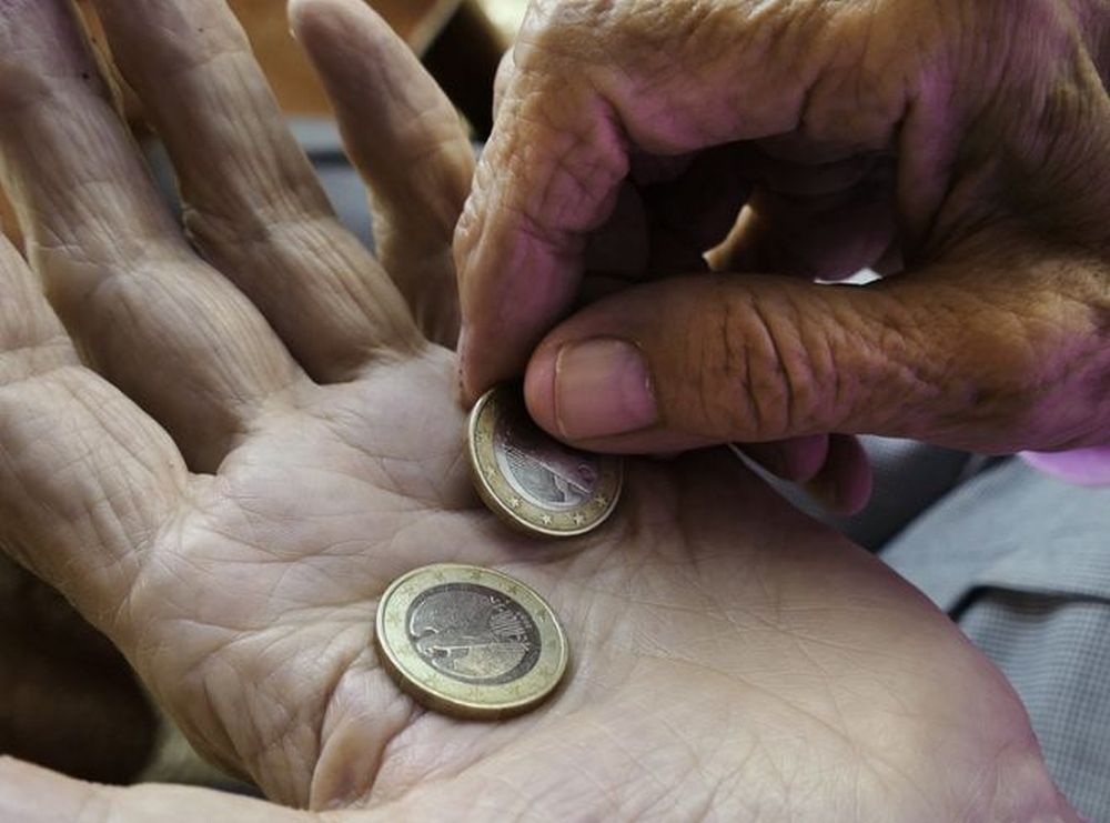 le mani di un anziano con due monete da 1 euro su un palmo