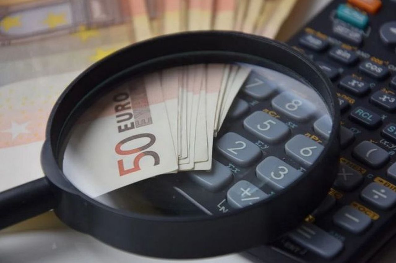 una calcolatrice inquadrata da una lente di ingrandimento insieme ad alcune banconote da 50 euro