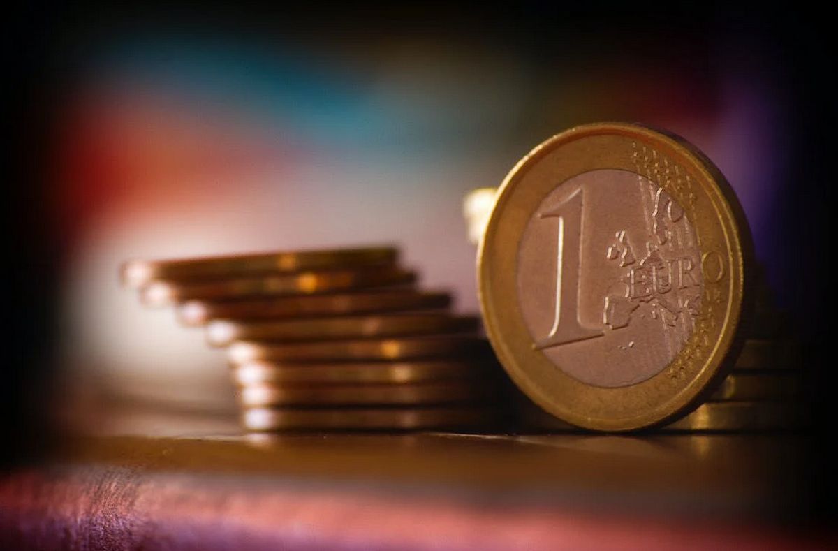 una moneta da un euro posata di taglio su un piano accanto ad altre monete incolonnate