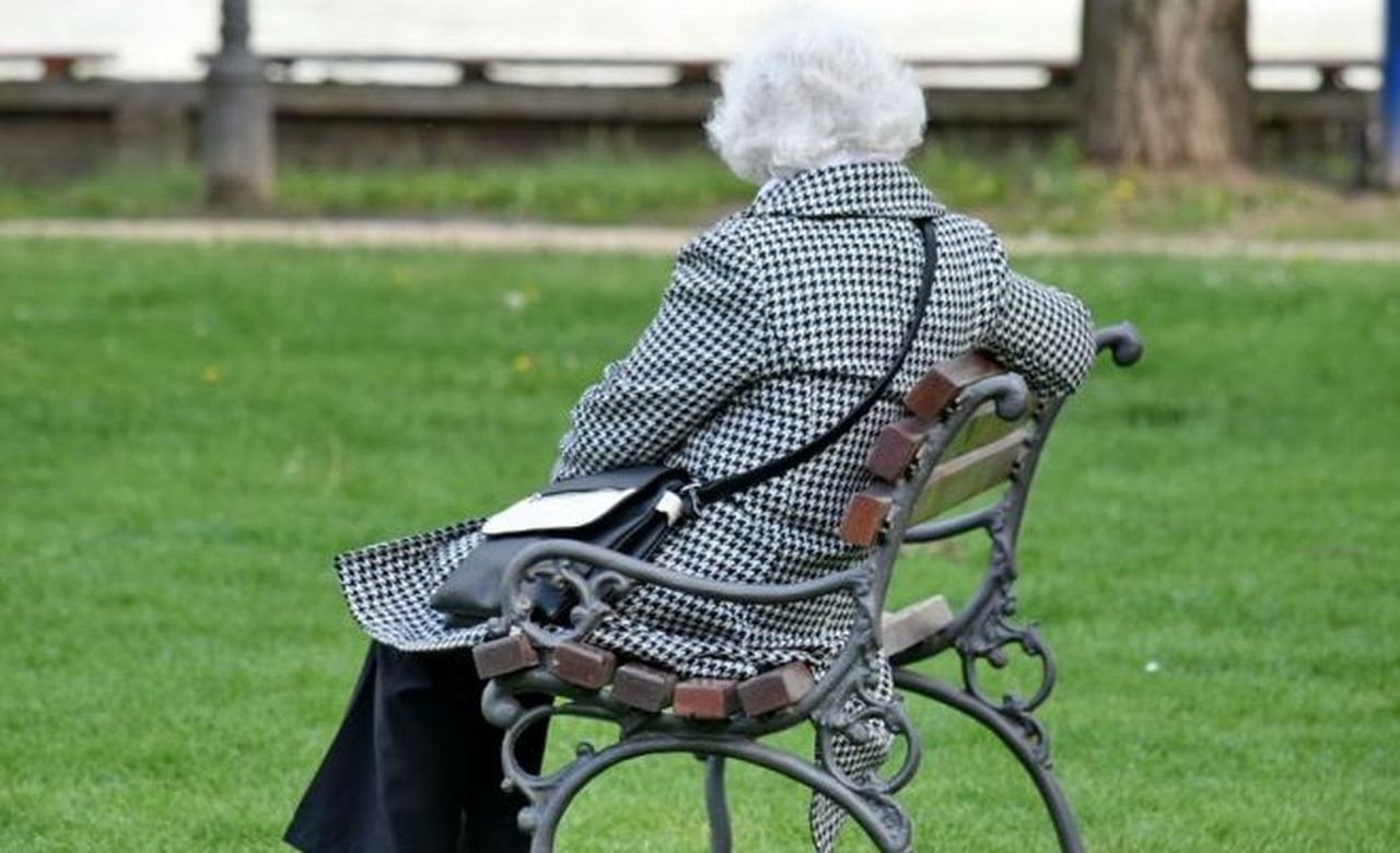 una signora anziana che siede su una panchina in riva al lago