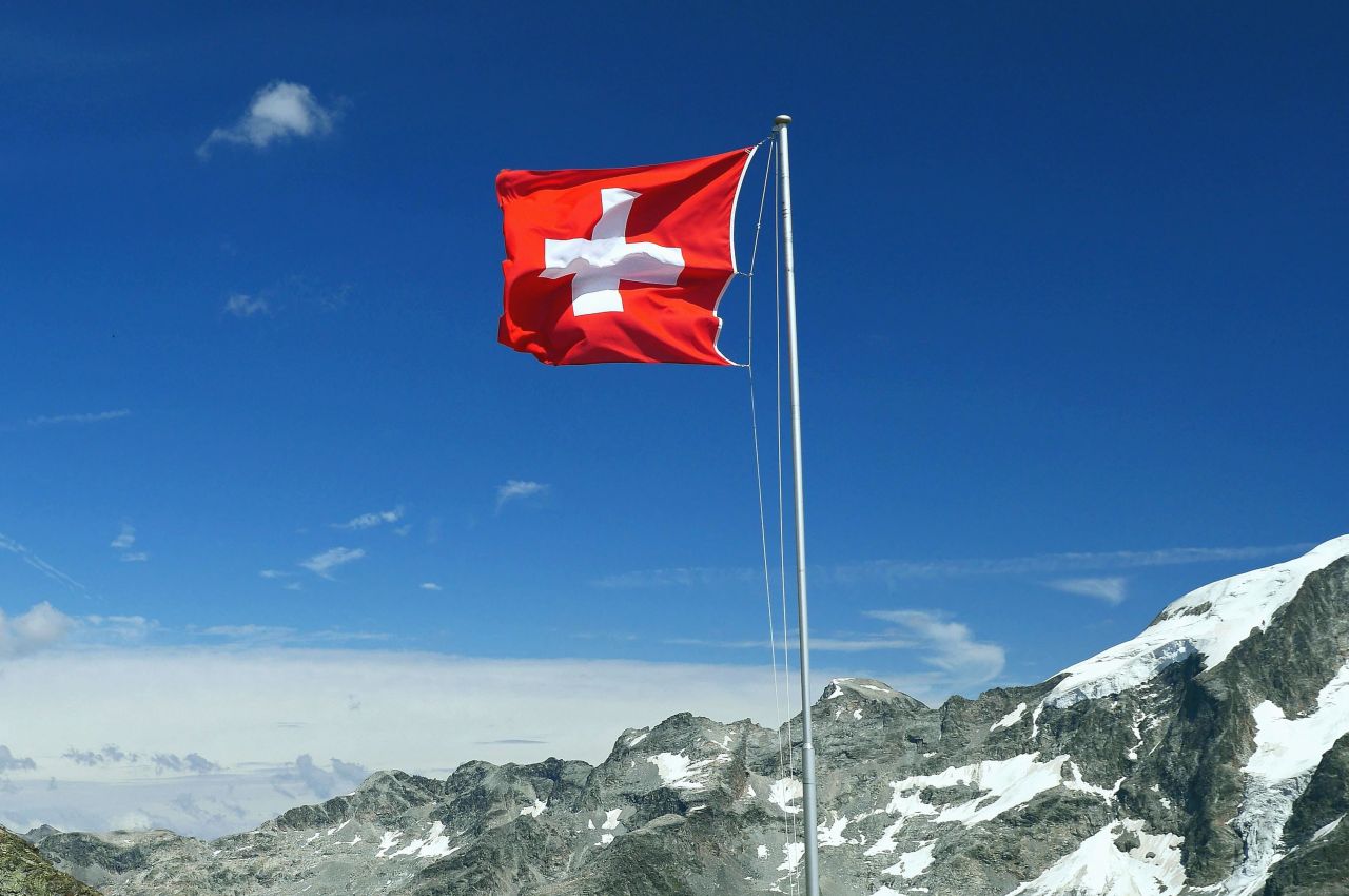 la bandiera della Svizzera che si staglia nel cielo azzurro oltre vette innevate