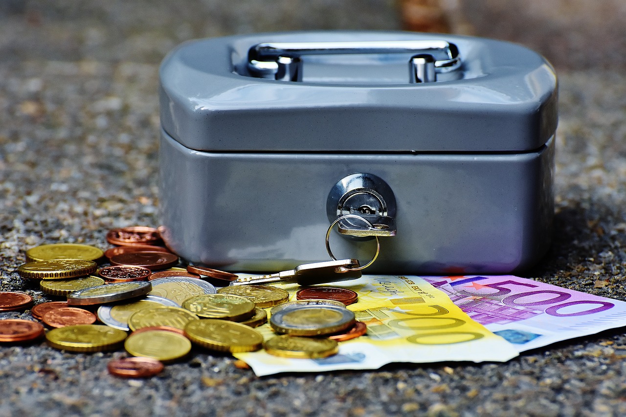 un cofanetto di metallo poggiato su un piano con alcune monete e banconote di euro