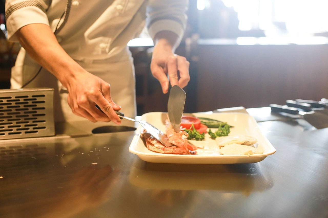 il bancone di una cucina con una portata e le mani dello chef che curano i dettagli