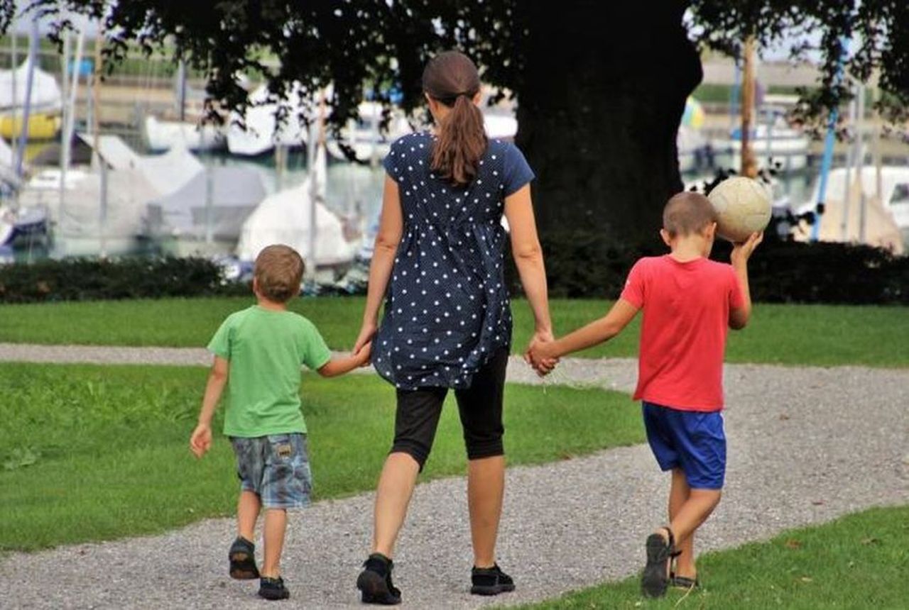una mamma che passeggia al parco tenendo per mano i due figli