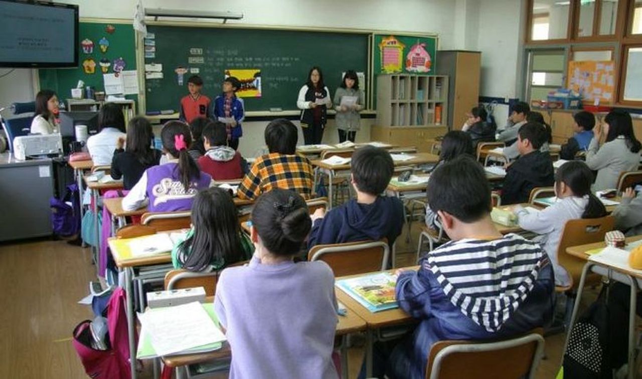 un'aula di scuola con alunni seduti ai banchi e l'insegnante alla cattedra