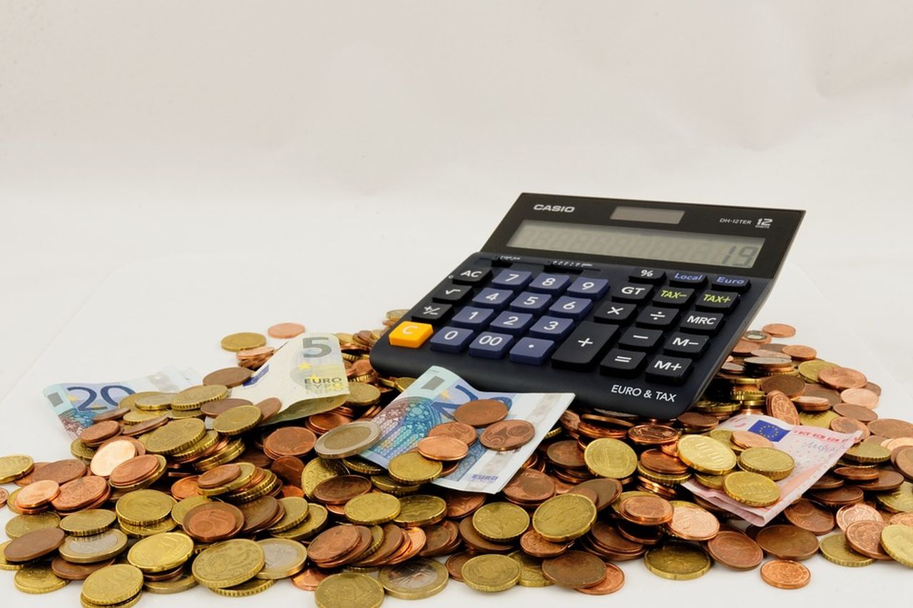 calcolatrice poggiata su mucchieto di monete con qualche banconota