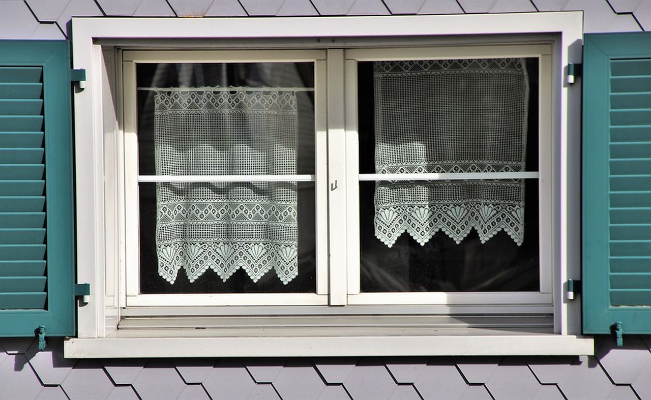 una finestra con persiane aperte e tendine bianche all'interno