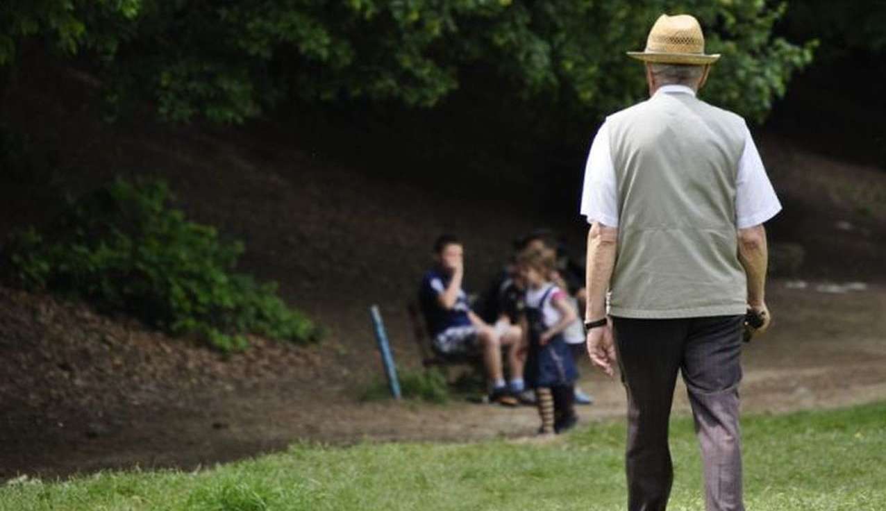 un signore anziano inquadrato di spalle mentre passeggia in un parco