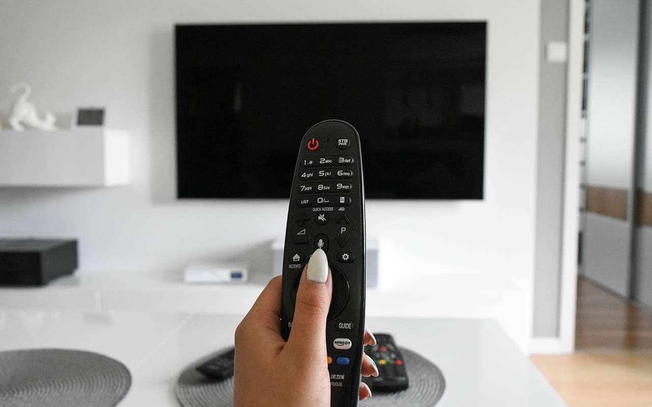 la mano di una donna con il telecomano puntato verso un televisore spento