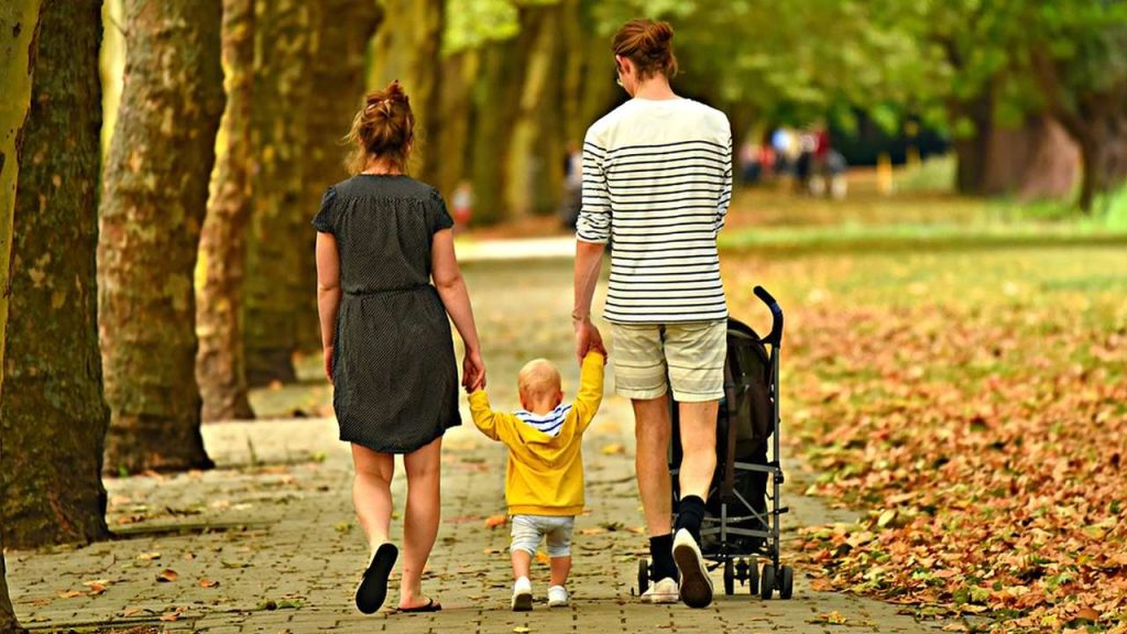 padre e madre a passeggio in un parco tenendo per mano il figlio piccolo