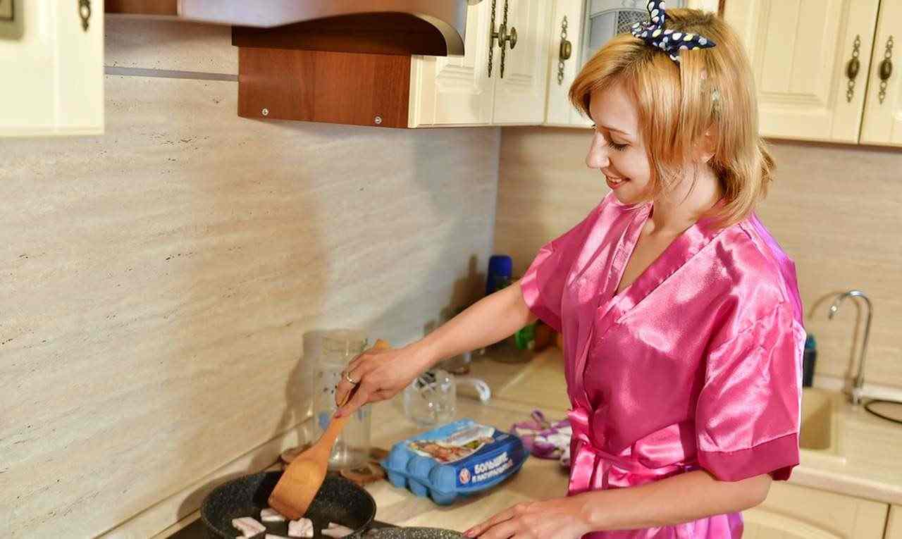 giovane casalinga ai fornelli con vestaglia rosa satinata