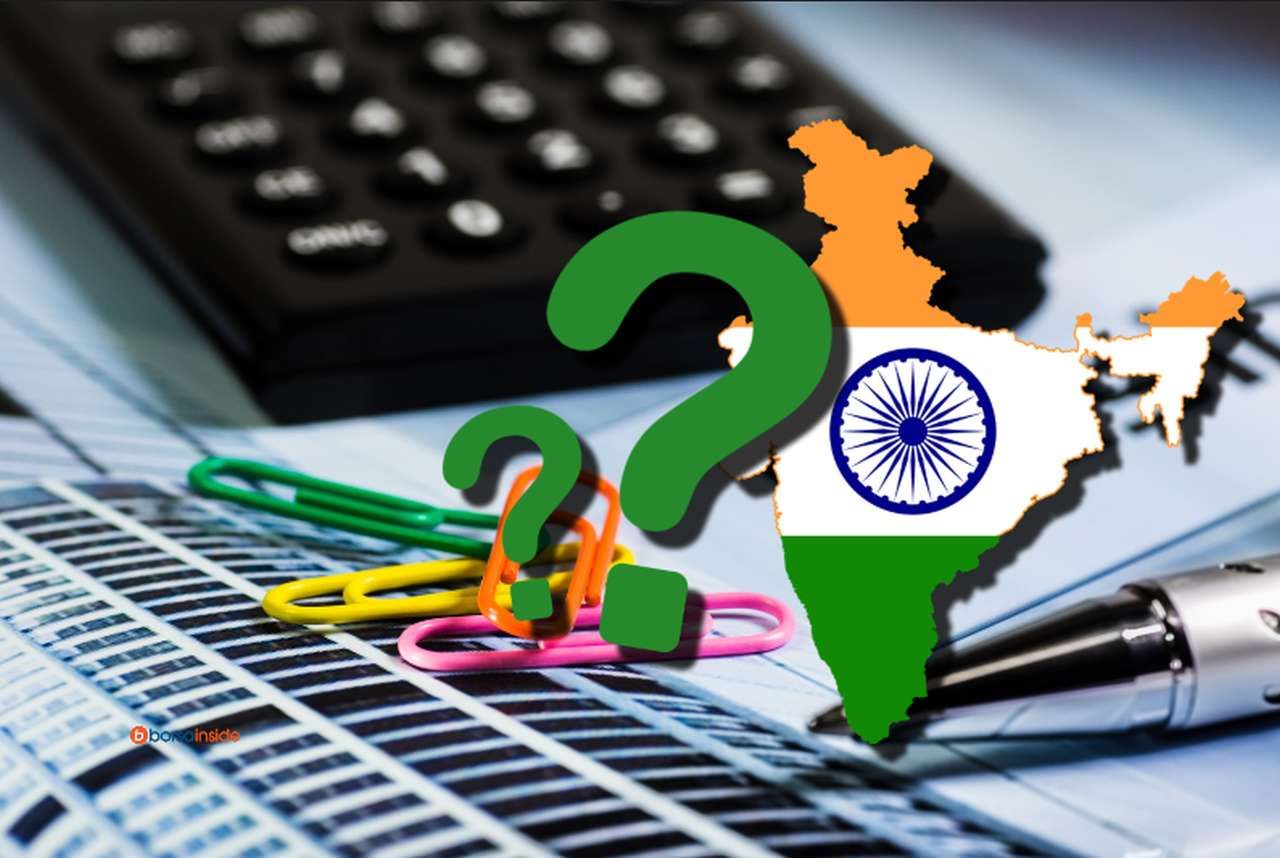 una calcolatrice con dei documenti e una penna su un piano, con la bandiera dell'India e dei punti interrogativi in sovrimpressione