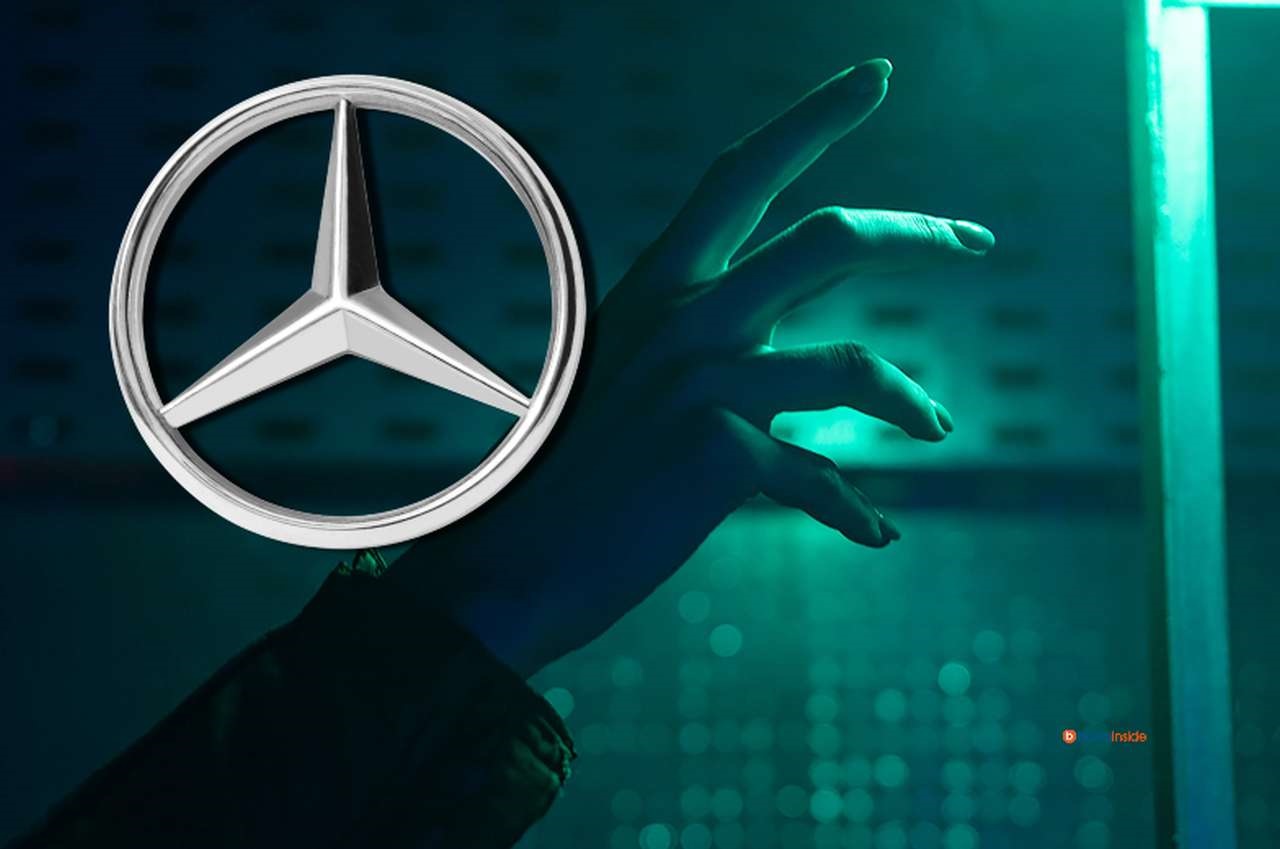 una mano tesa verso una tenue luce azzurrina su uno sfondo scuro. In alto a sinistra il logo della Mercedes