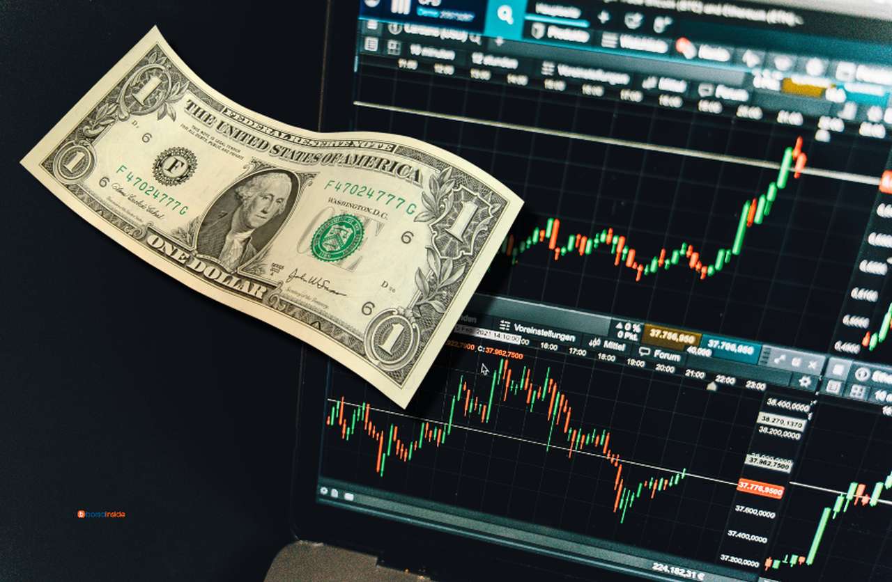 dei grafici finanziari sullo schermo di un laptop e una banconota da un dollaro in sovrimpressione