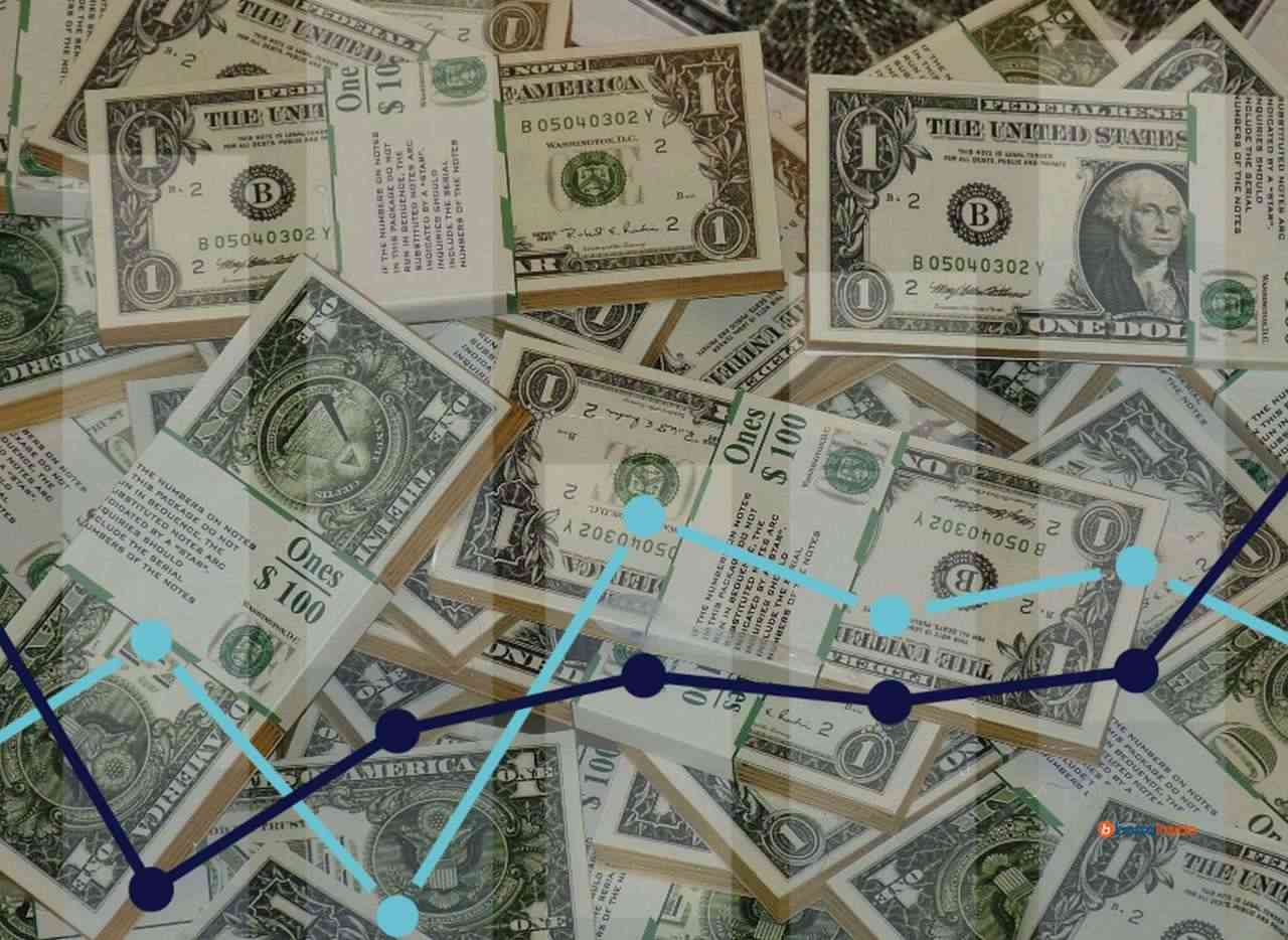 un grafico a colonne con svariate mazzette di banconote in dollari che tappezzano lo sfondo