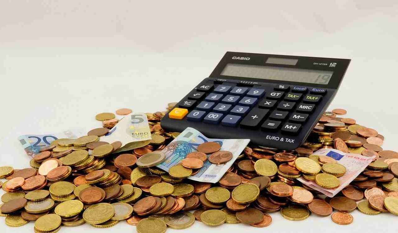 calcolatrice poggiata su mucchieto di monete con qualche banconota