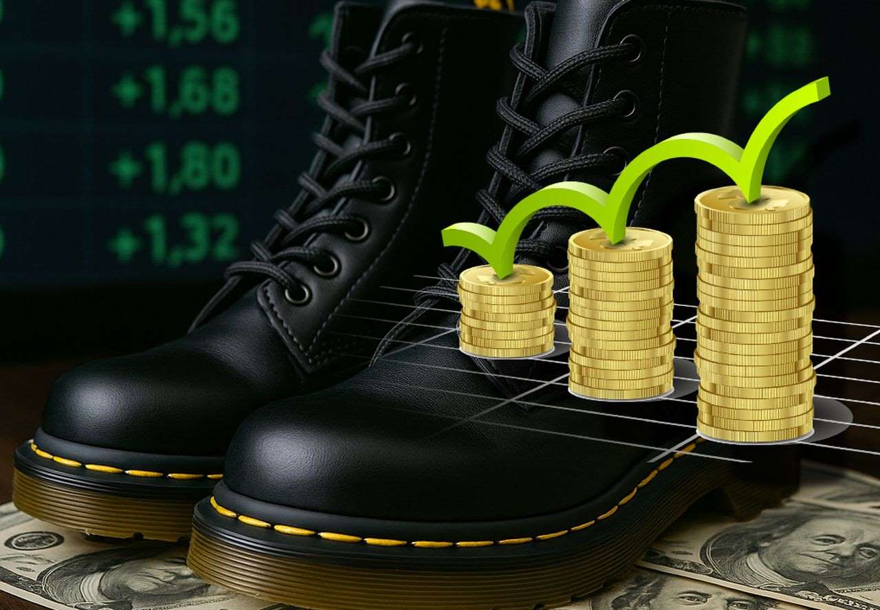 un paio di anfibi Dr Martens poggiati su alcune banconote. In sovrimpressione delle pile di monete