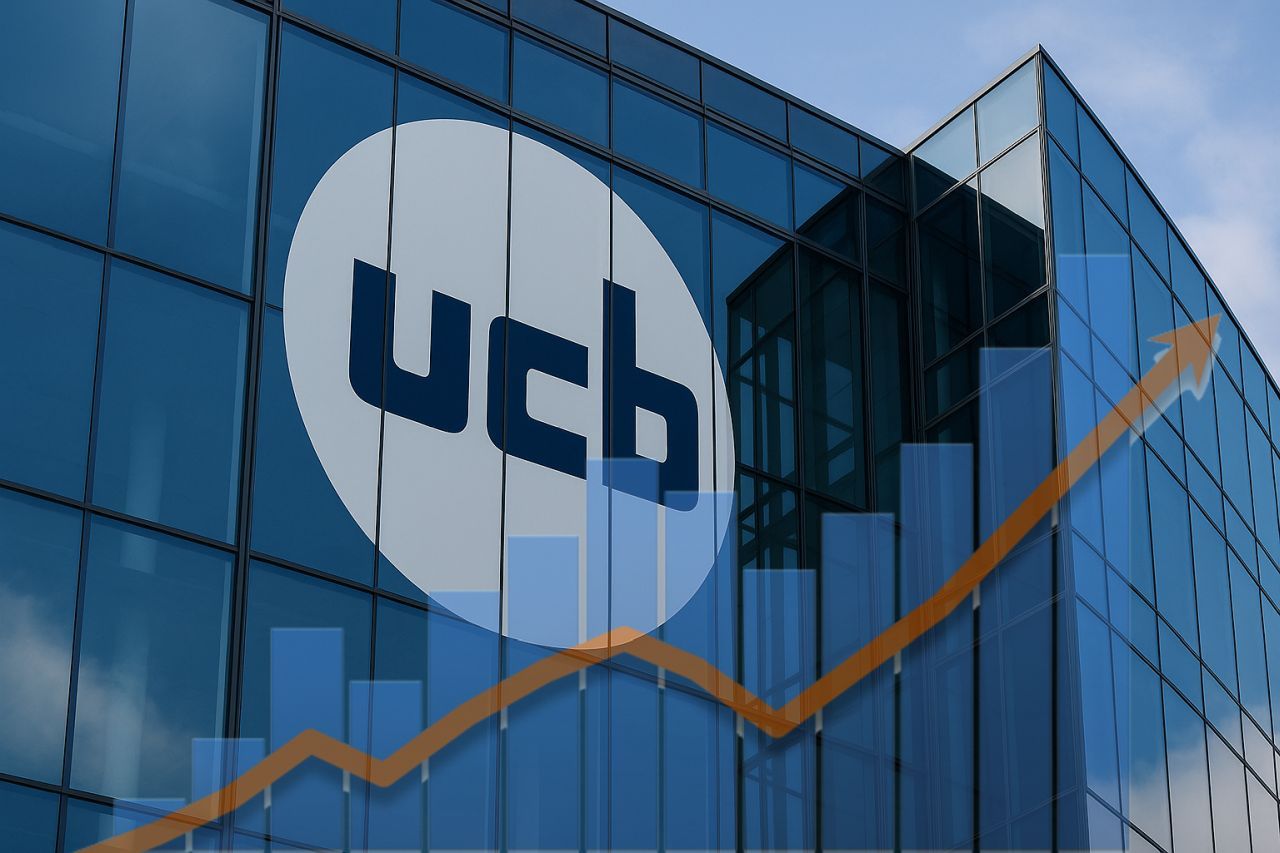 Un palazzo di vetro con il logo Ucb sulla facciata. In sovrimpressione, in trasparenza, un grafico a colonne con una freccia verso l'alto