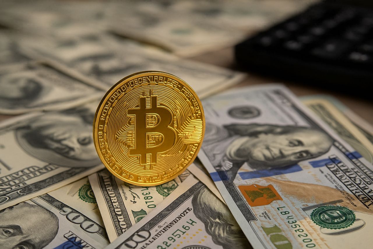 una moneta con il simbolo di Bitcoin poggiata di taglio su alcune banconote