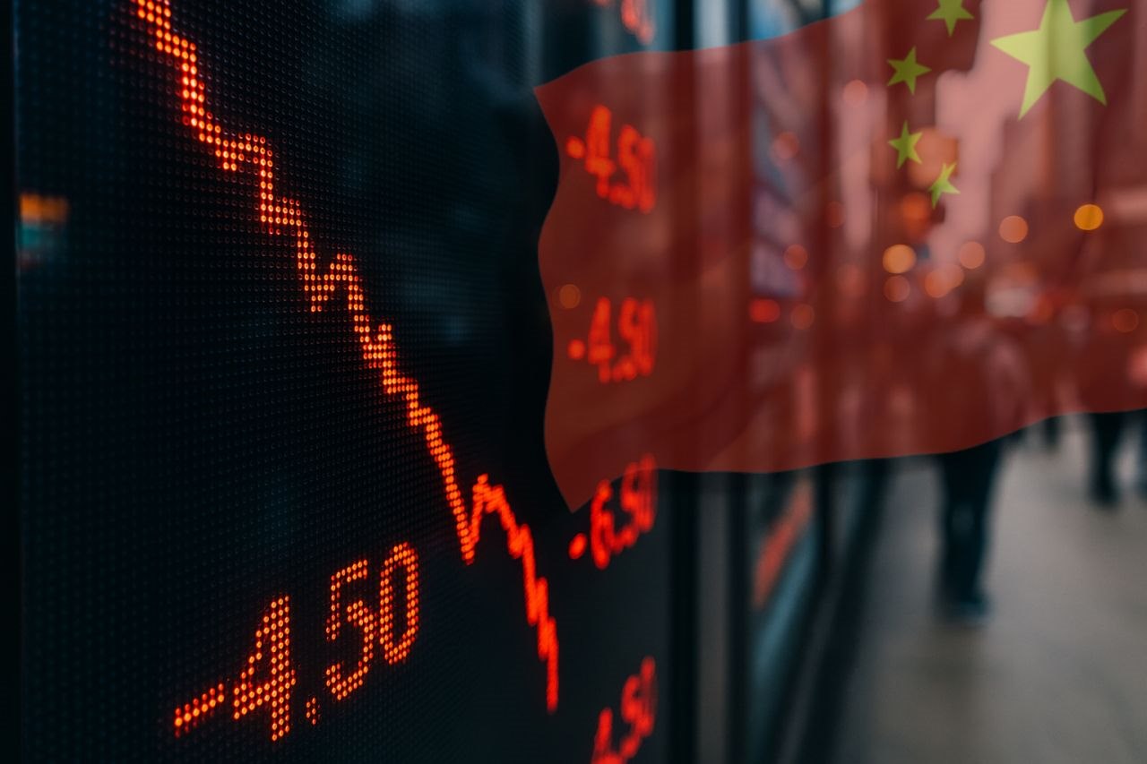 Un grafico finanziario in discesa e la bandiera della Cina in alto a destra in trasparenza