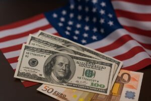 Alcune banconote in dollari e altre in euro con la bandiera degli USA sullo sfondo