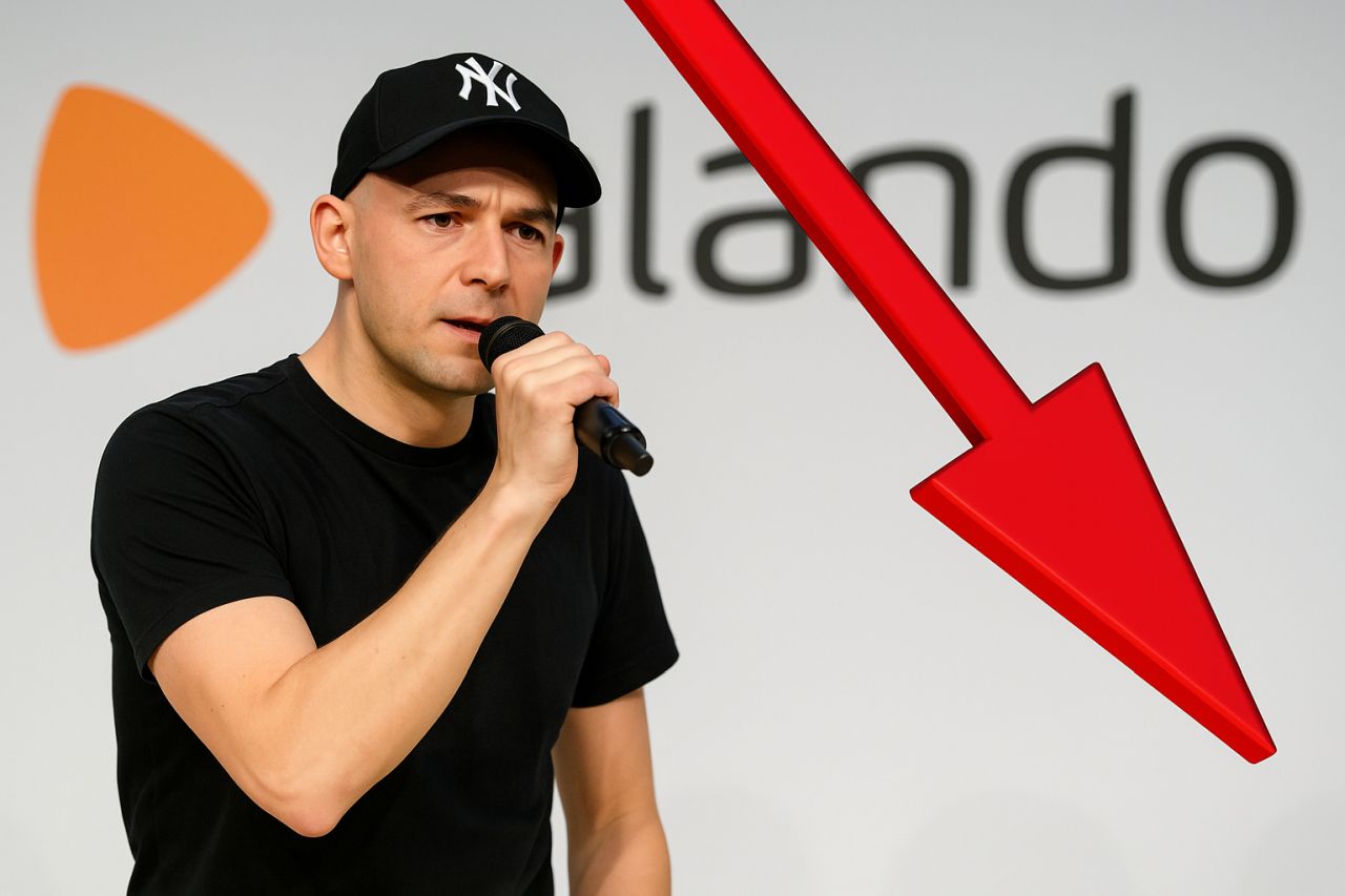Un uomo con t-shirt e berretto nero che tiene un microfono in mano. Sullo sfondo logo e scritta Zalando e una freccia rossa verso il basso