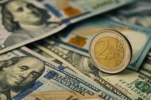 Una moneta da 2 euro con svariate banconote in dollari sullo sfondo