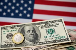 Banconote in dollari USA con una moneta da 1 euro davanti e la bandiera degli Stati Uniti sullo sfondo