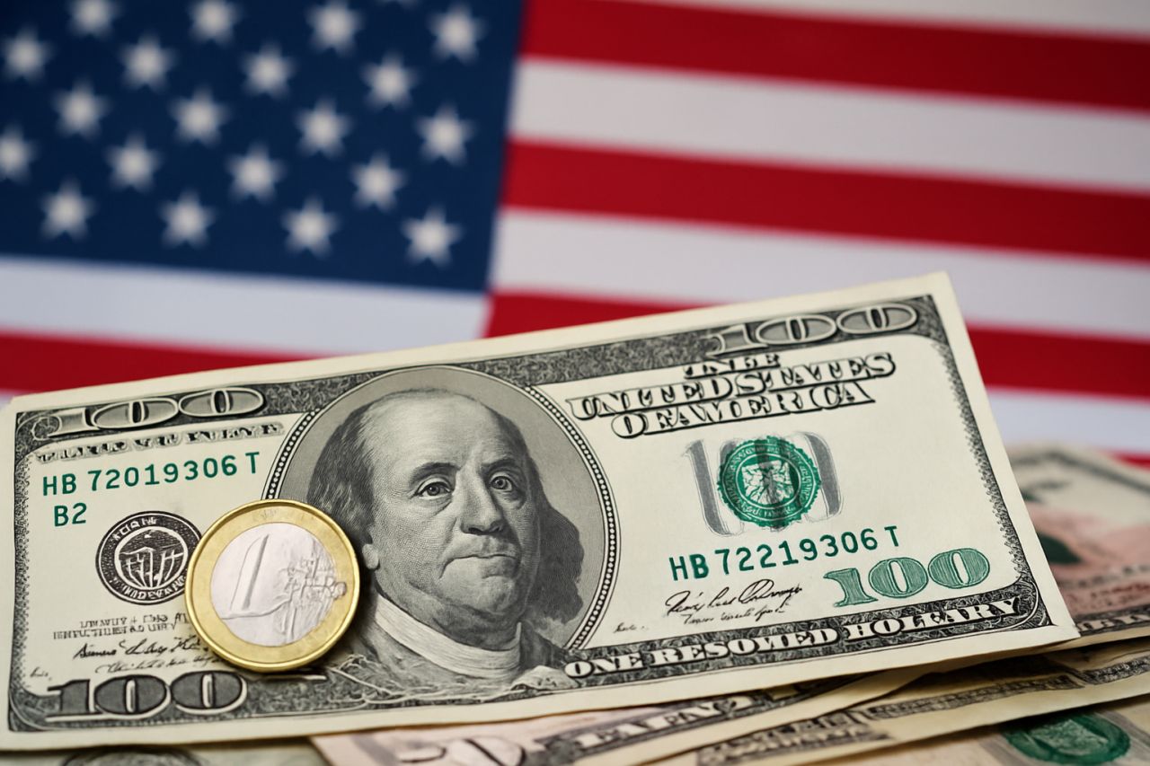 Banconote in dollari USA con una moneta da 1 euro davanti e la bandiera degli Stati Uniti sullo sfondo