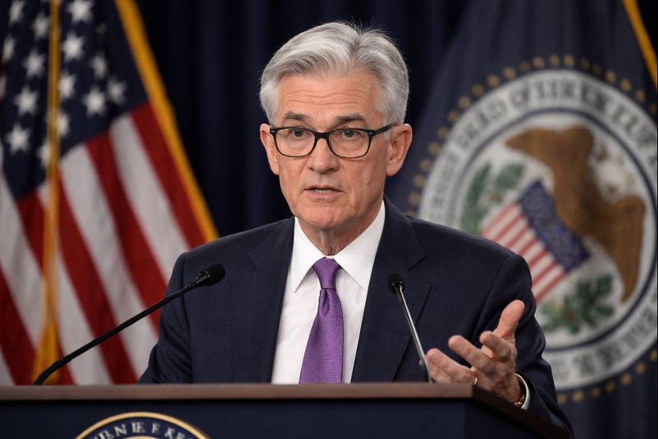 Primo piano di Jerome Powell con la bandiera degli USA e lo stemma della Fed alle spalle