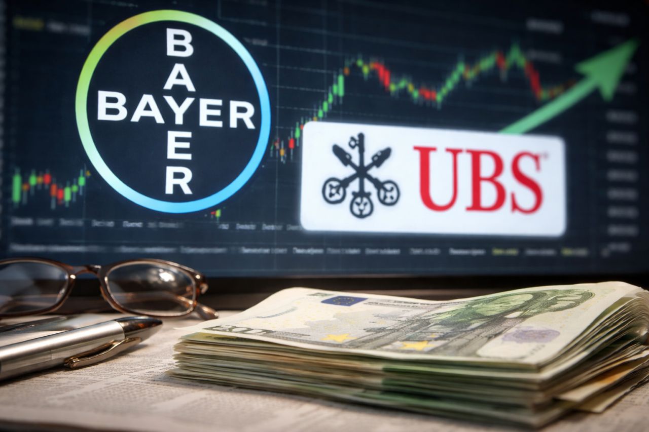 Scrivania con banconote in euro, occhiali e penna davanti a uno schermo con grafico di Borsa e loghi Bayer e UBS
